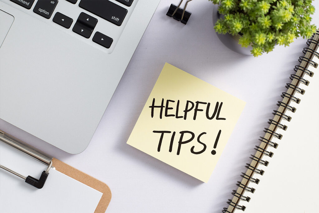 Sticky note with “Helpful Tips!” on a desk alongside a laptop, notebook, and plant—symbolizing effective advice for running a successful dental practice.