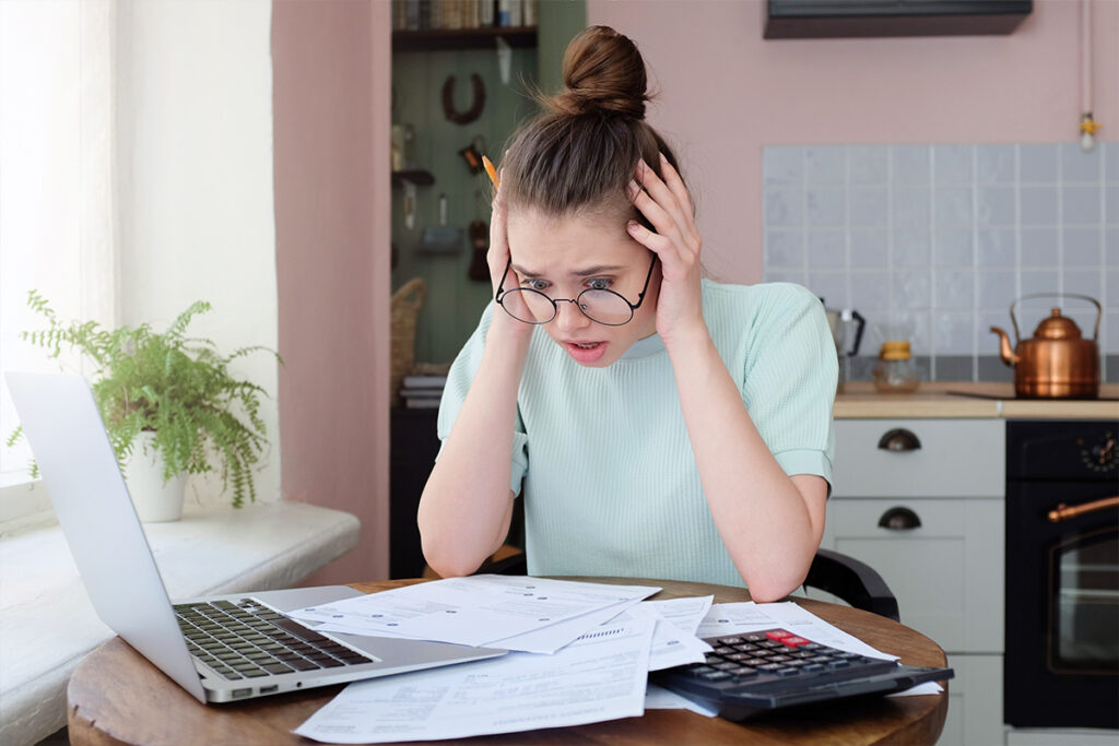 Stressed young woman surrounded by bills, calculator, and laptop at home, illustrating the emotional toll of poor financial planning.