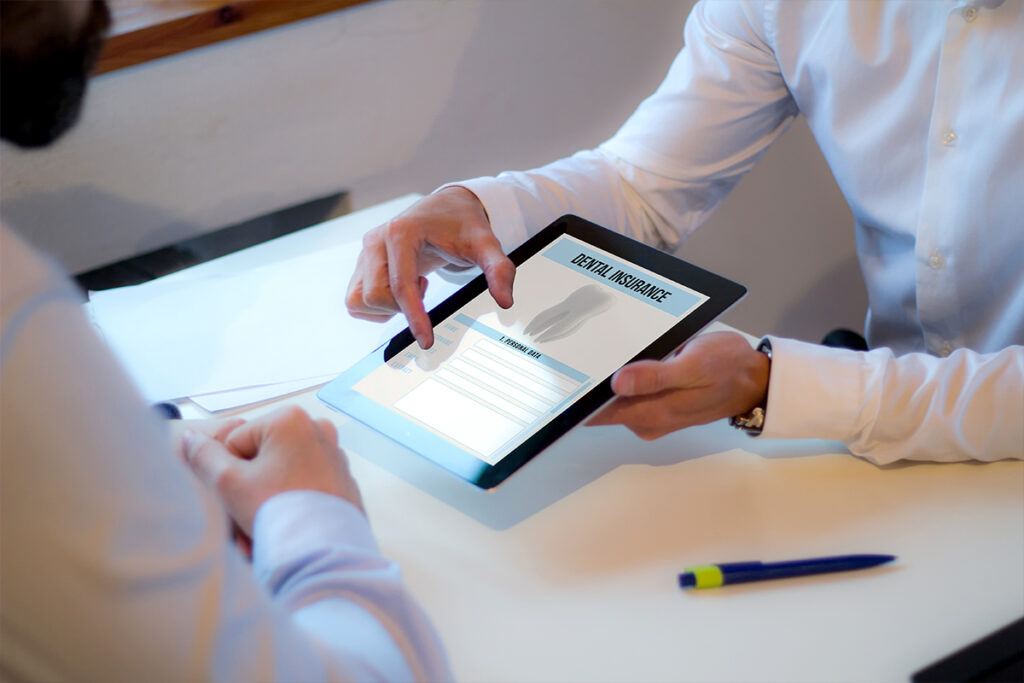 Two professionals reviewing dental insurance options on a tablet, highlighting the process of evaluating and selecting the right coverage.