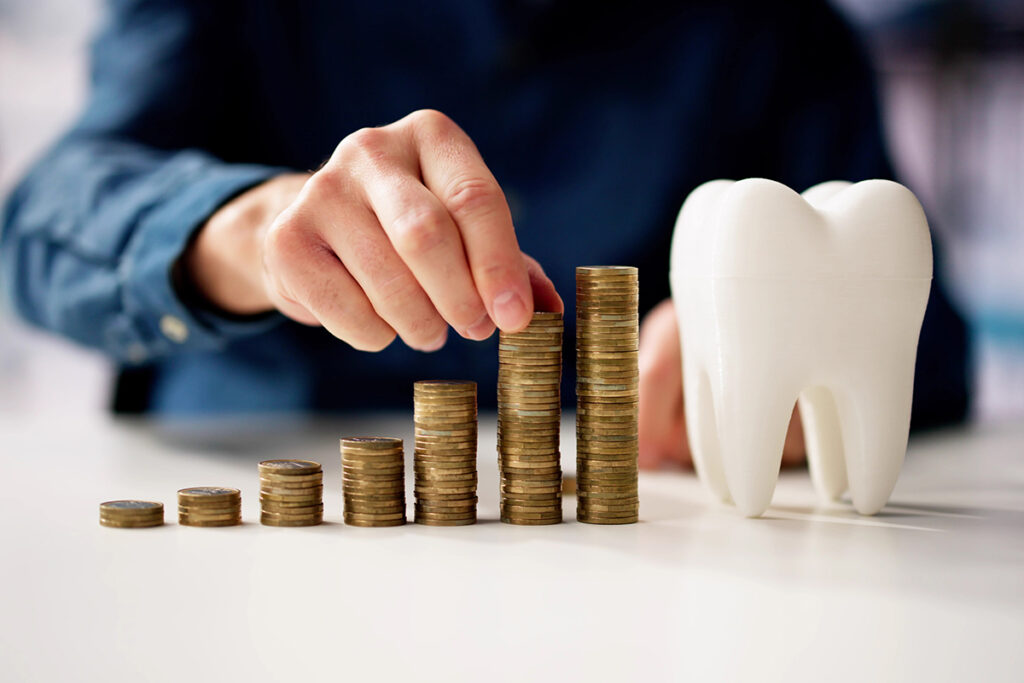 Stacked coins beside tooth model symbolizing rising dental costs and inflation impact.