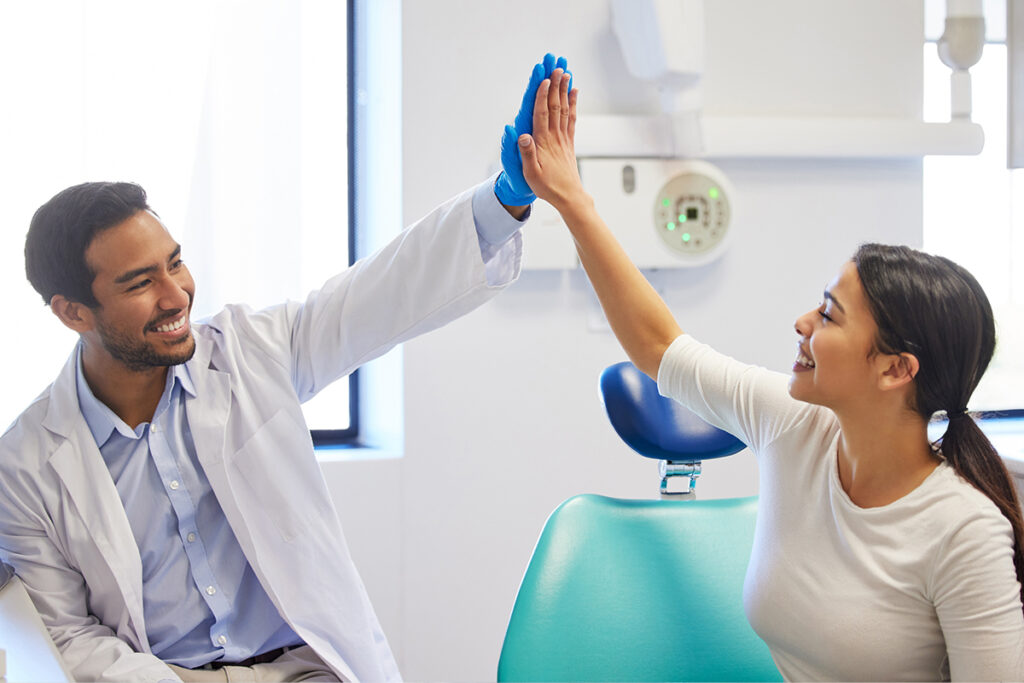Smiling dentist and patient giving a high-five in a dental office, representing a successful outcome from negotiating insurance fees.